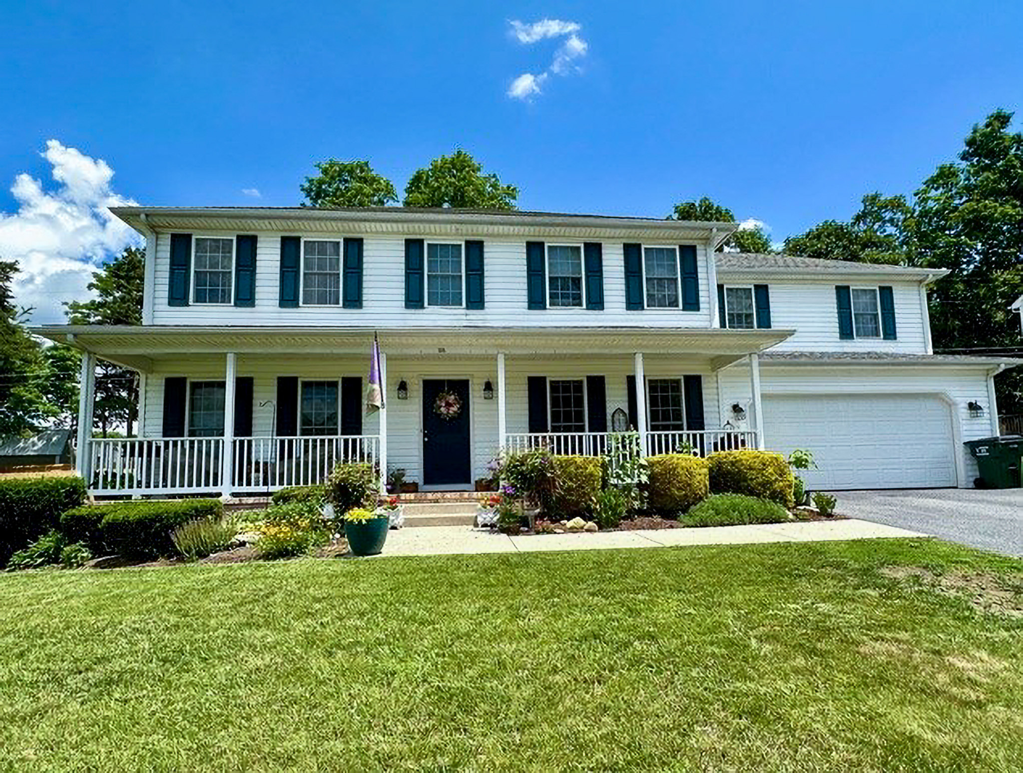 Two‑story white suburban house with black shutters, a wraparound front porch, landscaped shrubs, and a two‑car garage belonging to Sponsored Residential Providers Nancy and Zach Kaplan in Waynesboro, Virginia.