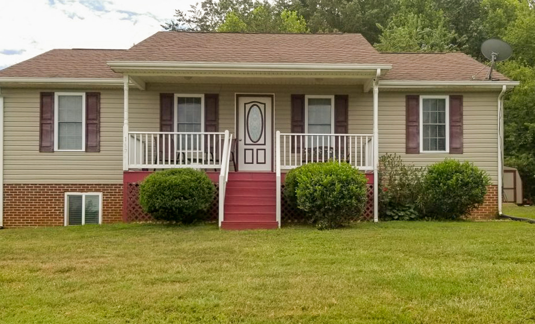 Single-story beige house with a red front porch, white railings, and neatly trimmed shrubs in the front yard belonging to Sponsored Residential Provider Calita Dillard in Lynchburg, Virginia.