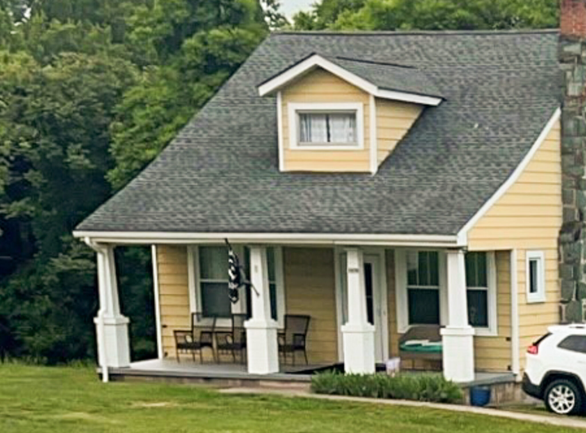 Yellow cottage-style house with a gray roof, front porch, white columns, and a small dormer window, set on a grassy lawn belonging to Sponsored Residential Provider Angie Elcox in Madison Heights, Virginia.