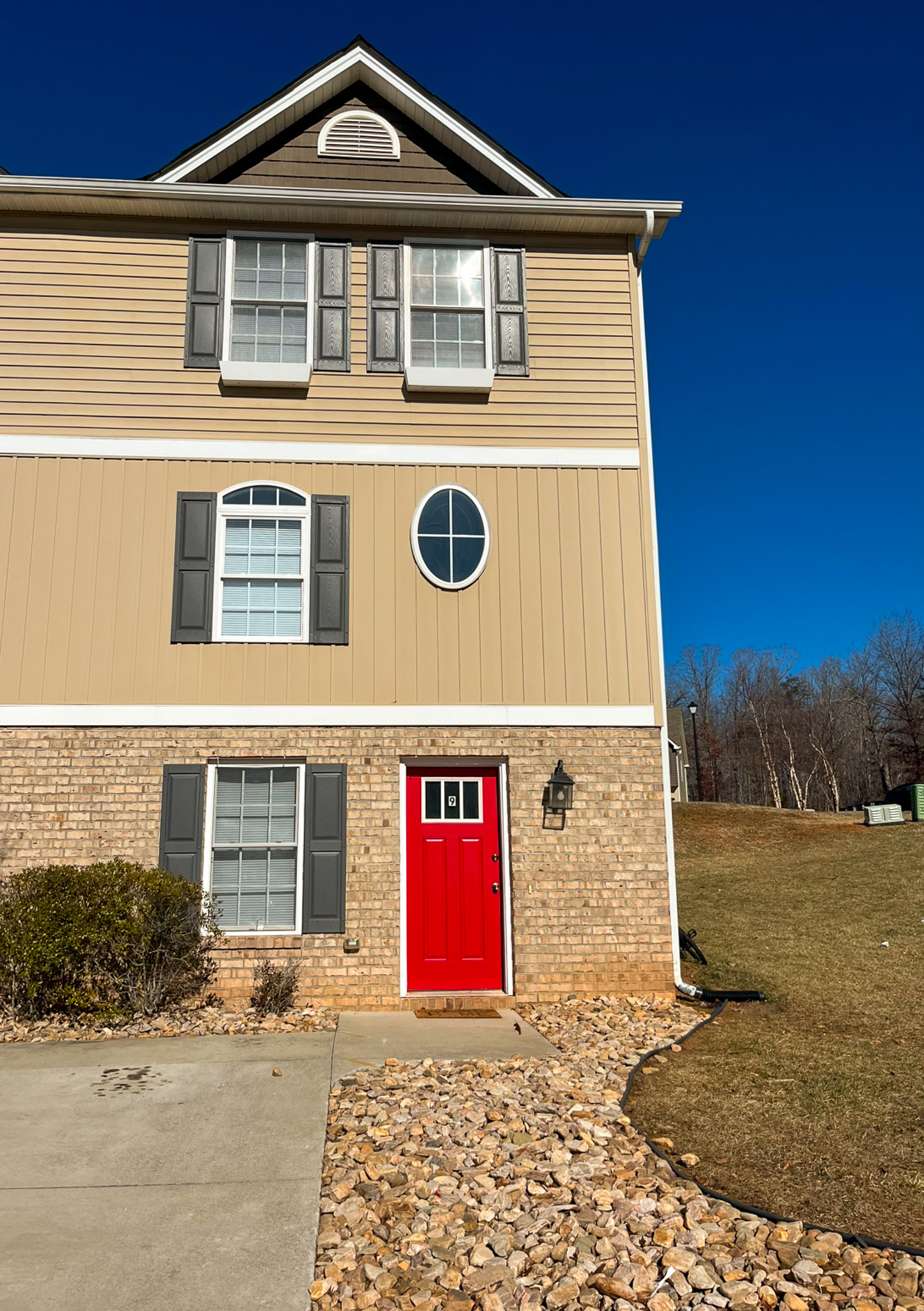 Three‑story beige townhouse with a bright red front door, stone landscaping, and a clear blue sky belonging to Sponsored Residential Provider Kanesha Moseley in Lynchburg, Virginia.