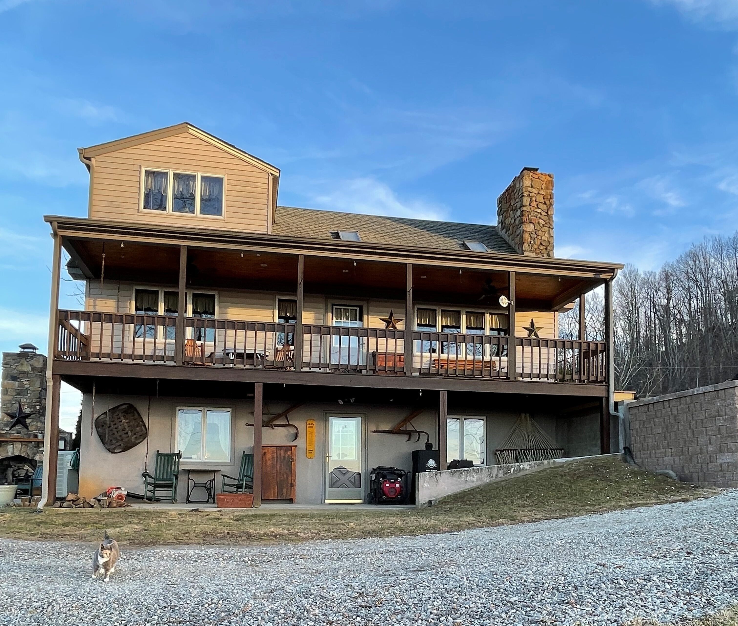 Two‑story cabin-style house with a large covered deck, wood railing, stone chimney, and a gravel driveway in front belonging to Sponsored Residential Providers Jimmy and Nancy Ayers in Monroe, Virginia.