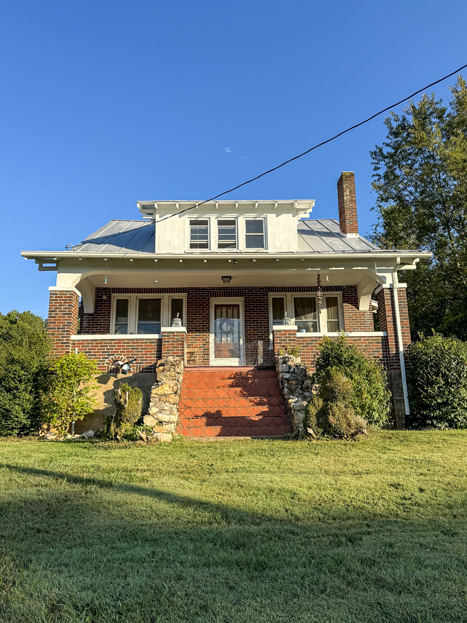 Brick house with white trim, a columned front porch, red brick steps, dormer windows, and a chimney, set on a grassy lawn belonging to Sponsored Residential Provider Tammy Hunt in Floyd, Virginia.