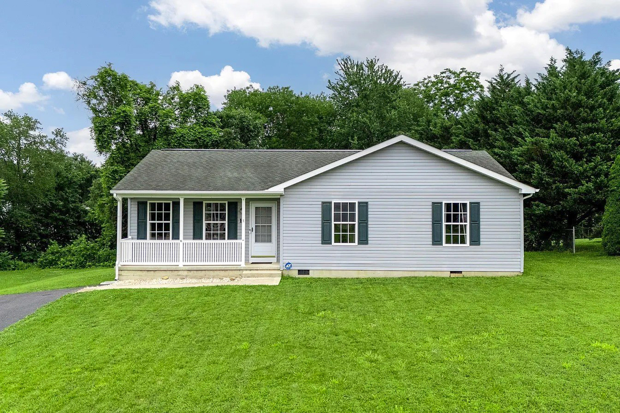 Single‑story white house with green shutters, a covered front porch, pitched roof, and a wide grassy yard belonging to Sponsored Residential Provider Gabrielle Straway in Grottoes, Virginia.