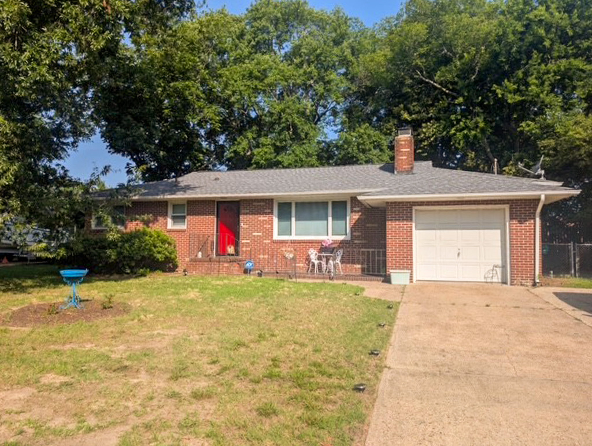 One‑story brick house with a red front door, attached garage, and a sloped lawn, backed by tall trees belonging to Sponsored Residential Provider Tammy Mitchell in Newport News, Virginia.