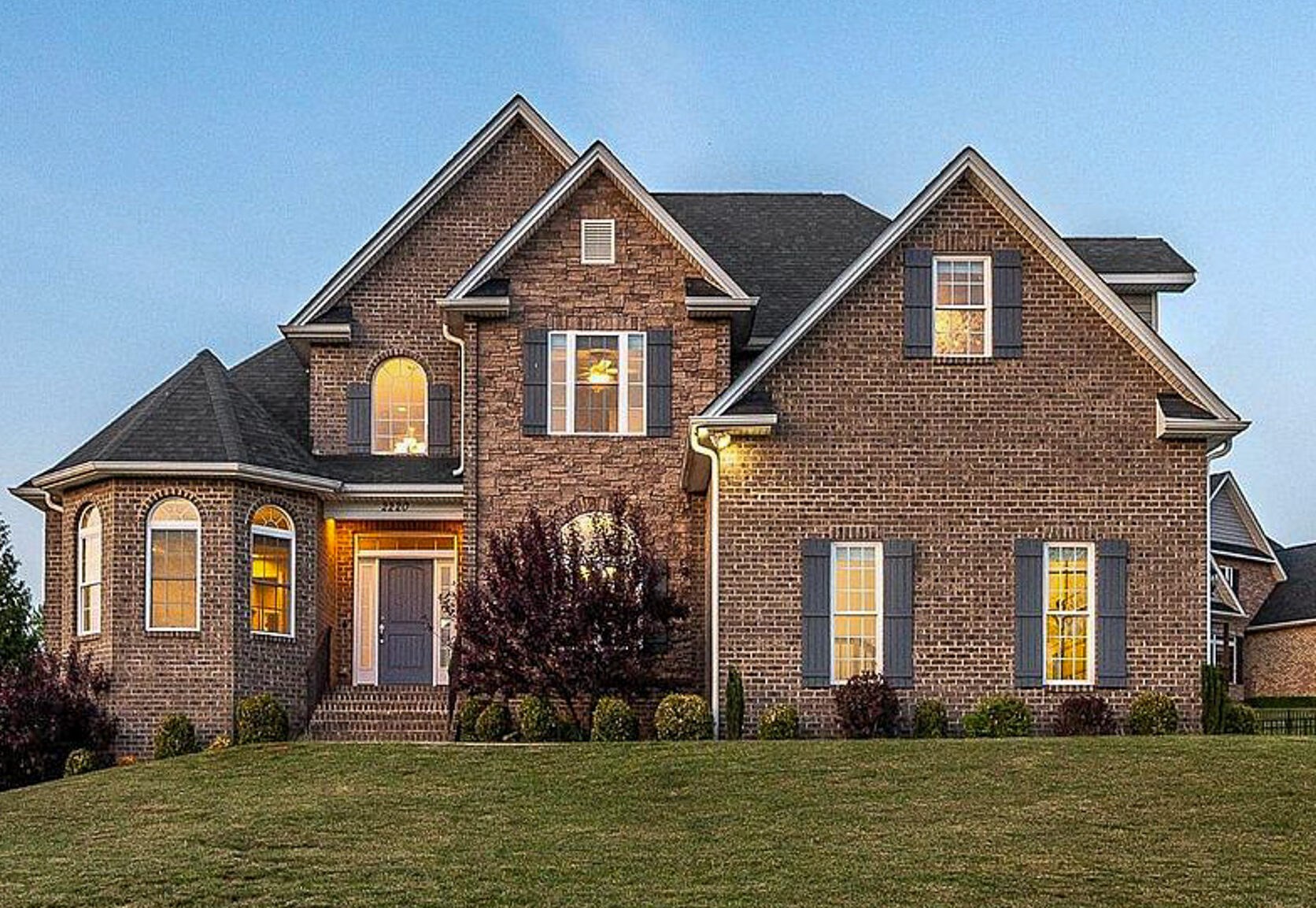 Two‑story brick house with multiple gables, large windows, and a neatly landscaped front yard at dusk belonging to sponsored residential provider Lisa Reed in Lynchburg, Virginia